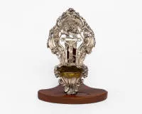 Holy water stoup, silver, 19th c., probably South German work, frame with rocaille and overhanging foliage, central relief of Christ's body on the cross, crowned by three putti, strongly projecting shell-shaped container, gilt interior, 26 cm high, 14 cm wide, approx. 182 g