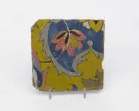Carreau safavide cuerda seca, Iran, seconde moitié du 17e s., pâte rouge clair, glaçures colorées bulleuses en jaune, bleu cobalt, vert et pourpre opaque, contours au manganèse, 20.7 x 20.7 cm, bords ébréchés, quelques bulles de glaçure ouvertes, surtout dans le pourpre.