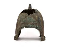 Bronzen helm, waarschijnlijk China of Noord-Chinees-Binnen-Aziatisch cultuurgebied, mogelijk Zhou- tot Han-periode, 1e millennium v.Chr. tot 1e millennium n.Chr., koperlegering, waarschijnlijk brons, gegoten; hoge, bijna halfbolvormige helmklok met uitgesproken radiale ribben en massief rechthoekig opengewerkt topornament, waarschijnlijk voor het bevestigen van een vroeger aanwezige helmversiering; in het onderste gedeelte aan beide zijden boogvormige velden en een rondlopende rij grote ronde bu