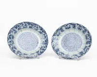 Paar Teller, China, Kangxi-Periode (1662-1722), Porzellan mit Unterglasurblau, im Spiegel stilisierte Blütenrosette mit Blattornamenten, die breite Fahne mit wechselnden Kartuschen floralen Dekors und gelapptem Rand, auf der Unterseite Doppelkreis mit...