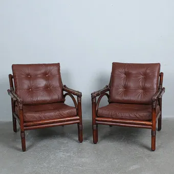 Paire de fauteuils lounge en bambou teinté et rotin avec coussins en cuir marron.