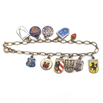 ANTIEKE CHARM ARMBAND VAN GOLD DOUBLE MET TIEN STADSWAPENS, VOORNAMELIJK ZILVER, EN EEN HART HANGER VAN 8 KARAAT GOUD MET KORAAL CA. 19CM, OMSTREEKS 1930.