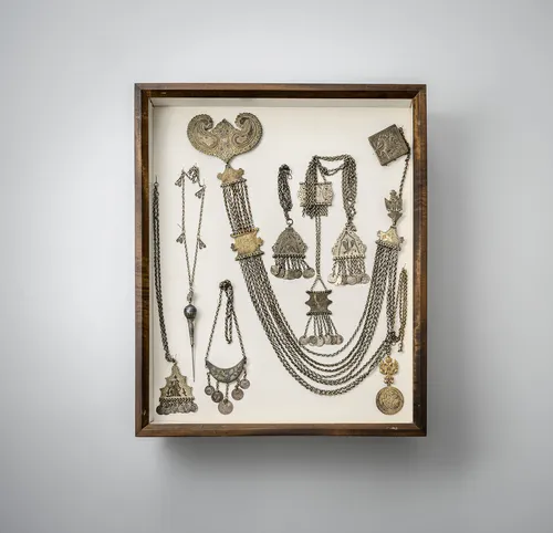 Group of jewellery, including necklaces, pendants and belts with earrings, partly silver, mounted in two glass cases