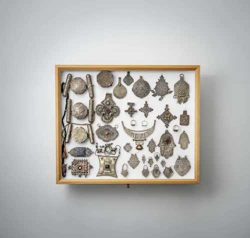 Group of jewellery, amulet boxes, pendants and chain jewellery, partly silver, mounted in two glass cases