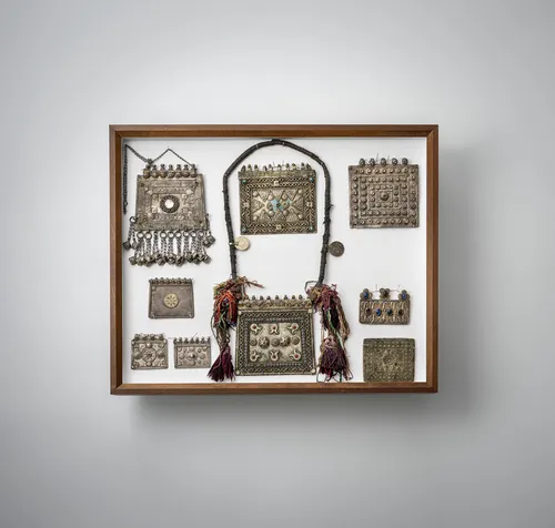 Groep sieraden, o.a. oorbellen, plaquettes en borstsieraden, deels van zilver, gemonteerd in drie glazen kasten