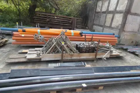 Sada bednicích a lešenářských doplňků, mimo jiné trubky a bednicí svěrky, na skladovacím stojanu