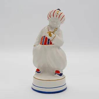 OSKAR BURKHARDT. ORIËNTAALS BEELD "TURK", ERNST TEICHERT GMBH (OOK BEKEND ALS DEEL VAN DE MEISSEN OVEN- EN PORSELEINFABRIEK VOORHEEN CARL TEICHERT), JONGEN IN ORIËNTAAALSE KLEDING, STEENGOED, GEGLAZUURD, POLYCHROOM HANDSCHILDERWERK, DEELS MET GOUDDECOR, OMSTREEKS 1910.