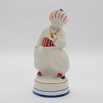 OSKAR BURKHARDT. ORIËNTAALS BEELD "TURK", ERNST TEICHERT GMBH (OOK BEKEND ALS DEEL VAN DE MEISSEN OVEN- EN PORSELEINFABRIEK VOORHEEN CARL TEICHERT), JONGEN IN ORIËNTAAALSE KLEDING, STEENGOED, GEGLAZUURD, POLYCHROOM HANDSCHILDERWERK, DEELS MET GOUDDECOR, OMSTREEKS 1910.