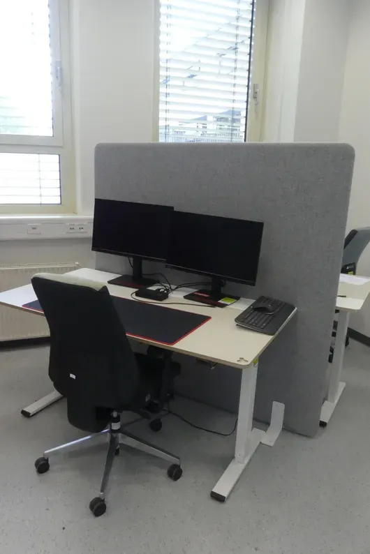 Electrically height-adjustable desk with office chair and partition, without contents