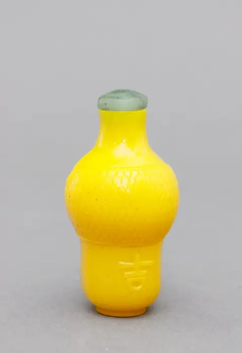 China, snuifdoos, Pekingglas, Qing, balustervorm in keizerlijk geel met ornamentreliëf en opschrift waarschijnlijk "Da Gù". Stop als afgeplatte bolvormige schijf van nephriet (of vergelijkbaar materiaal) met lepeltje