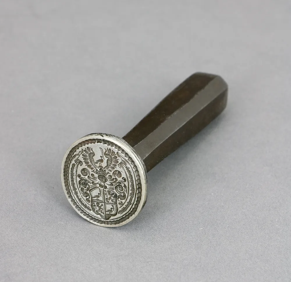 Pečeť s erbem, železo, 18. stol. 3,2 x 3 cm, d. 14,2 cm. Šlechtický erb se lvem a ptákem.
