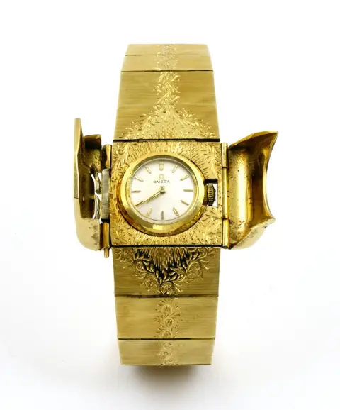 Montre, bracelet, or 18 carats, Omega, Suisse, vers 1960, mouvement Omega intégré dans le bracelet. Remontage manuel. Protection de montre à double clapet. Couvercle et bracelet gravés. Bracelet avec fermoir à clip et deux sécurités. Poinçonné K18. Cadran et couronne signés. L 18,7 cm. Poids brut 67 g. Fonctionne, durabilité non testée.